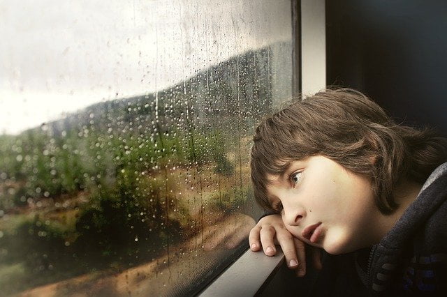 jongen staart uit raam en voelt zich onzeker